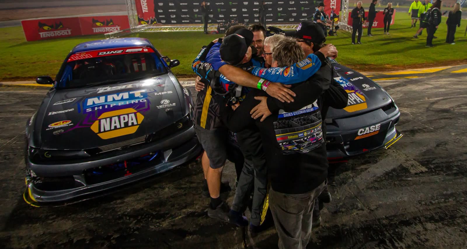 The Team DSR crew embracing between both championship cars after the 2026 title win at Mercury Baypark